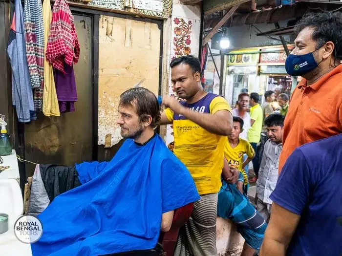 Tourist getting a haircut at a streetside barbershop in Dhaka, Bangladesh